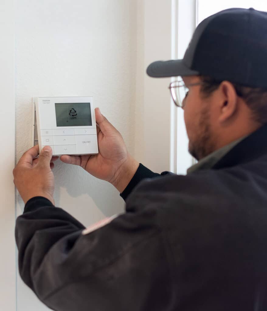 A technician installing a thermostat on a wall.