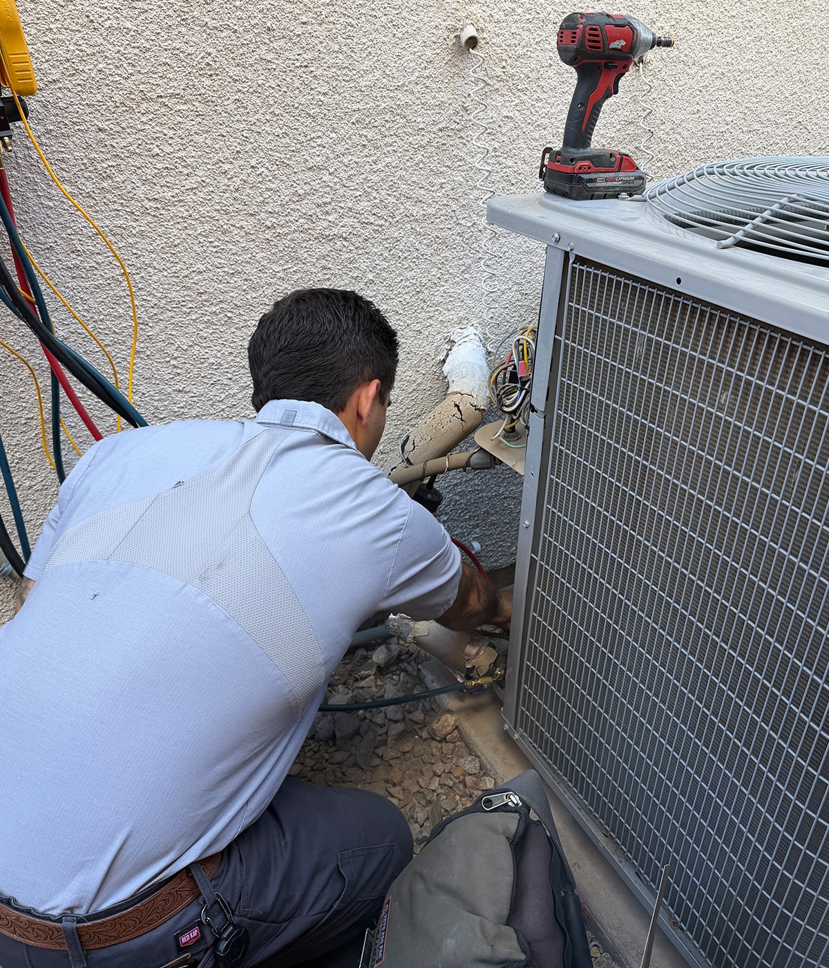 Sunrise HVAC technician kneeling to repair wiring and connections on an outdoor air conditioner condenser unit