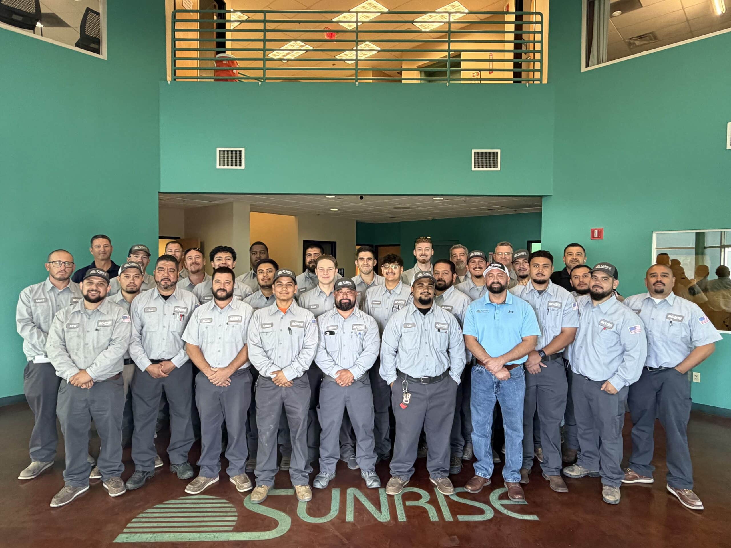 he full sunrise hvac team gathers for a group photo in the lobby, standing over the company's sunrise logo painted on the floor