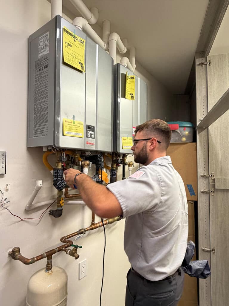 Technician installing two Rinnai tankless water heaters in utility closet