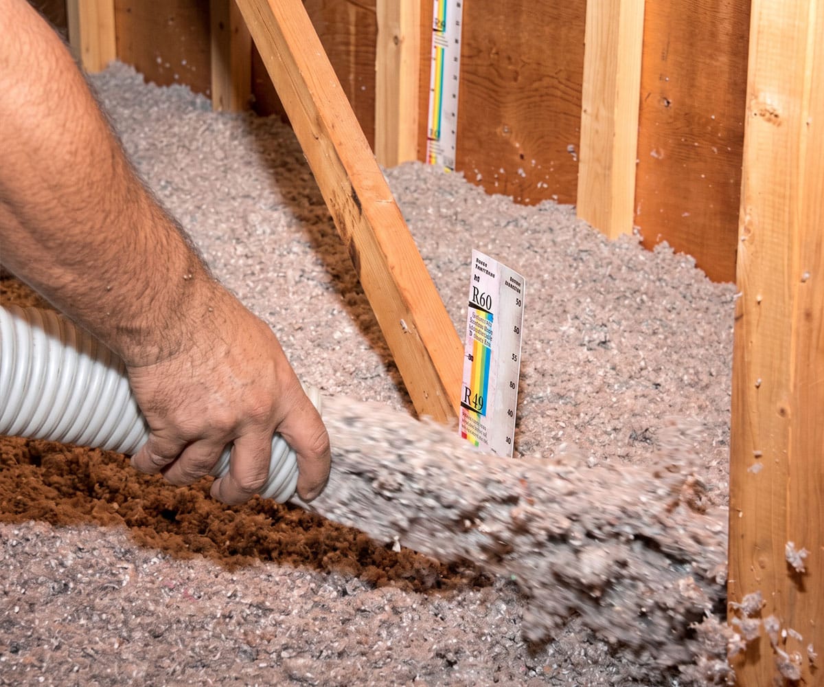 Installer blows loose-fill insulation past R49 and R60 depth rulers in a Henderson attic for Sunrise Service.